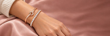 Rose gold love knot bangle stacked with a tennis bracelet on the wrist
