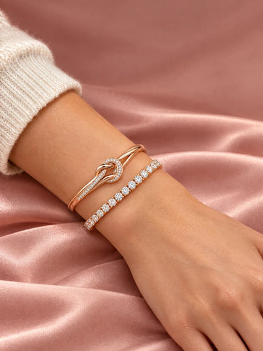 Rose gold love knot bangle stacked with a tennis bracelet on the wrist